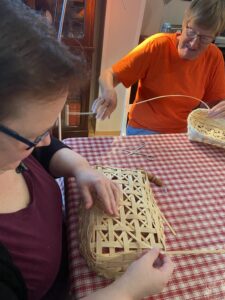 Two women make bread baskets together at a kitchen table