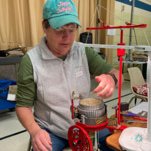 A seated woman uses a sock cranking machine.